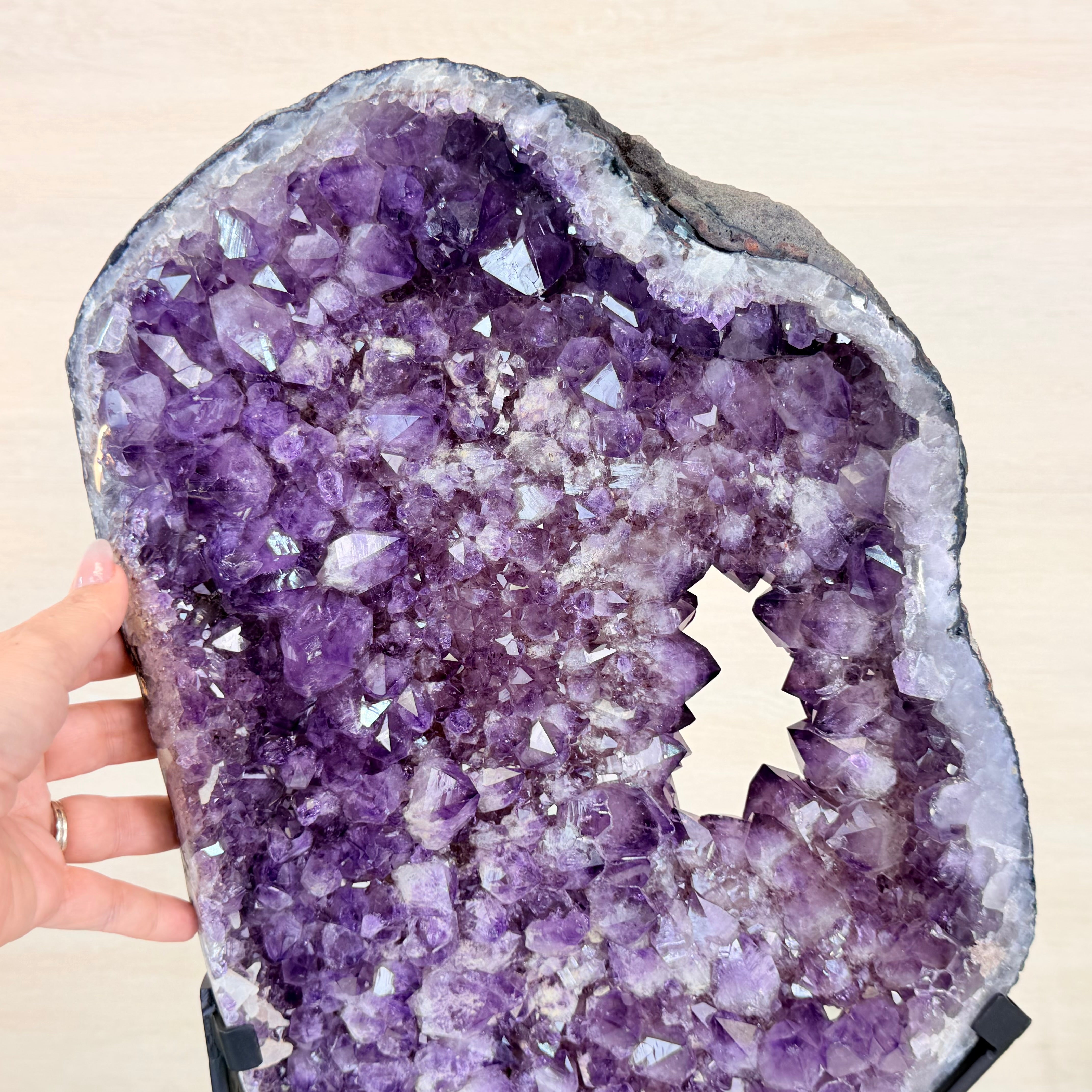 Amethyst crystal geode held by a hand on a beige background