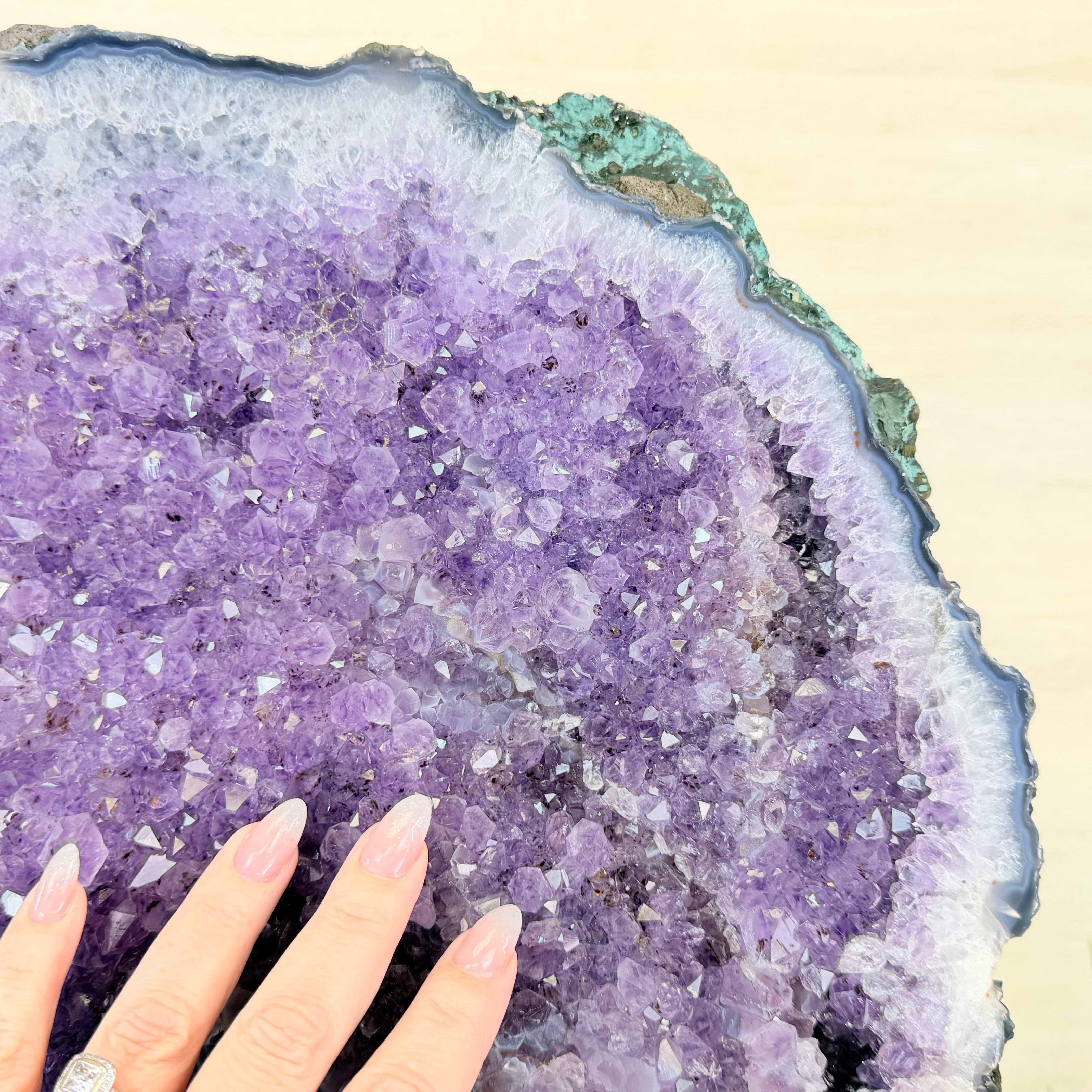 Close-up of a purple crystal geode with a hand for scale on a beige background