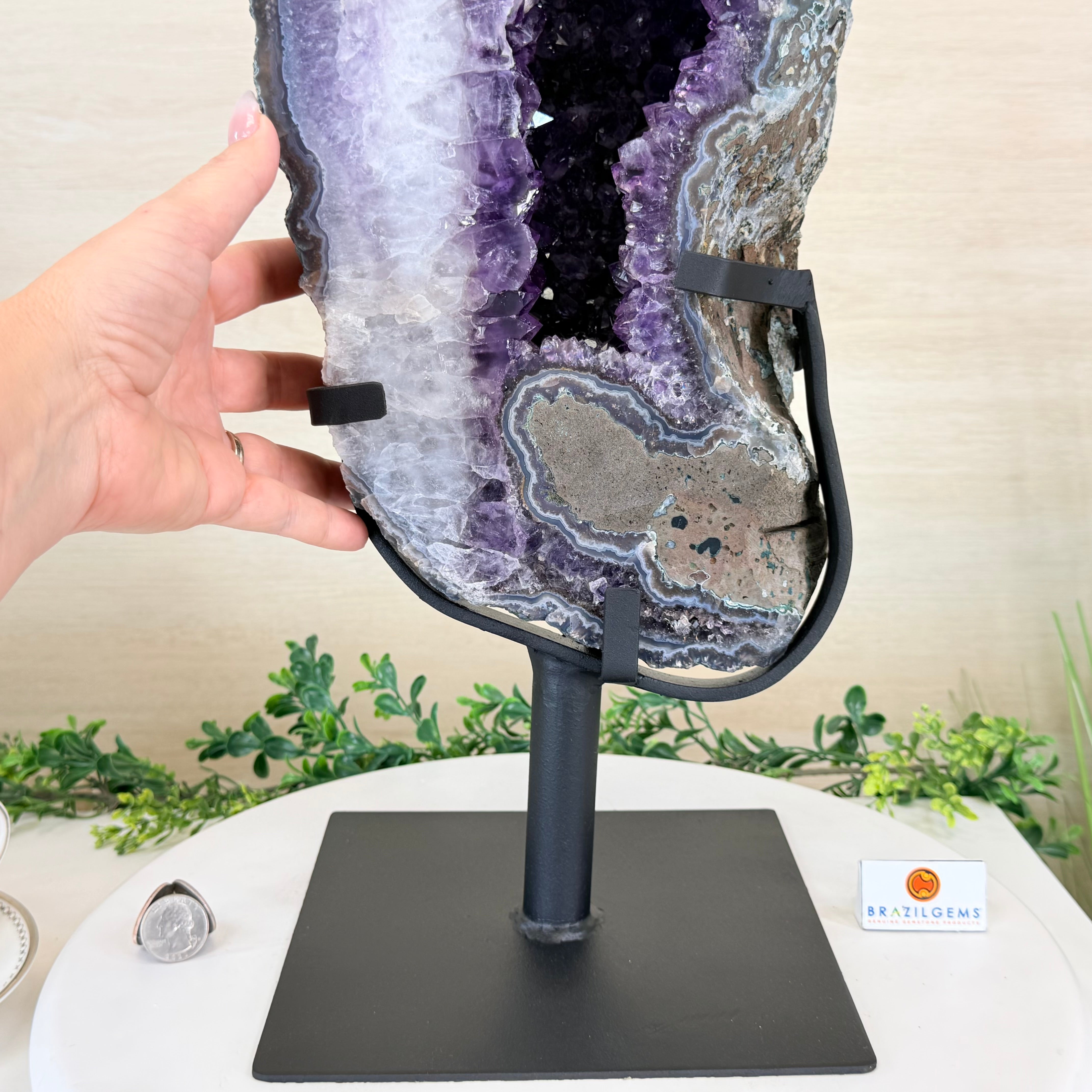 Amethyst geode on a stand with a hand adjusting it, against a neutral background.