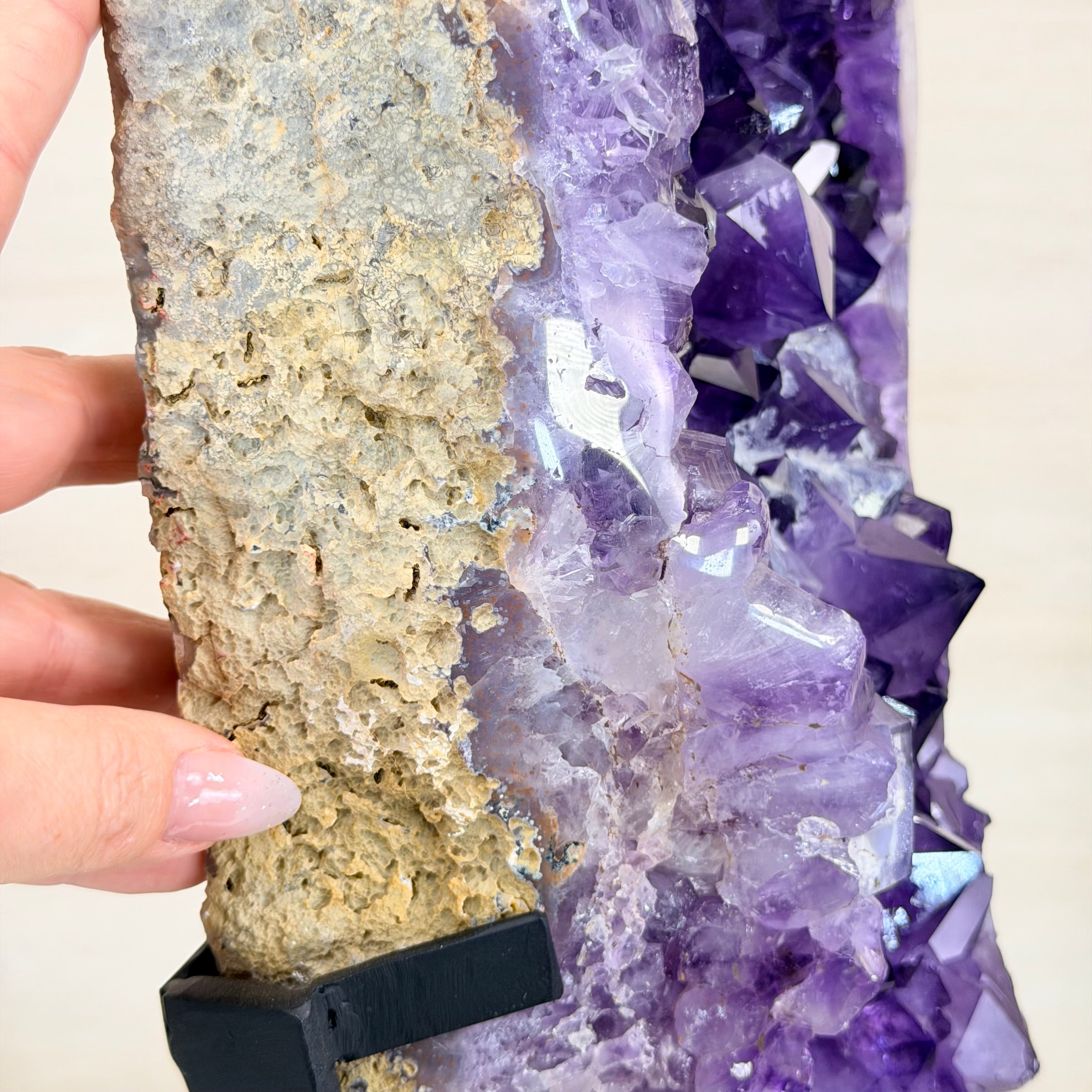 Amethyst crystal cluster with a hand holding it against a neutral background