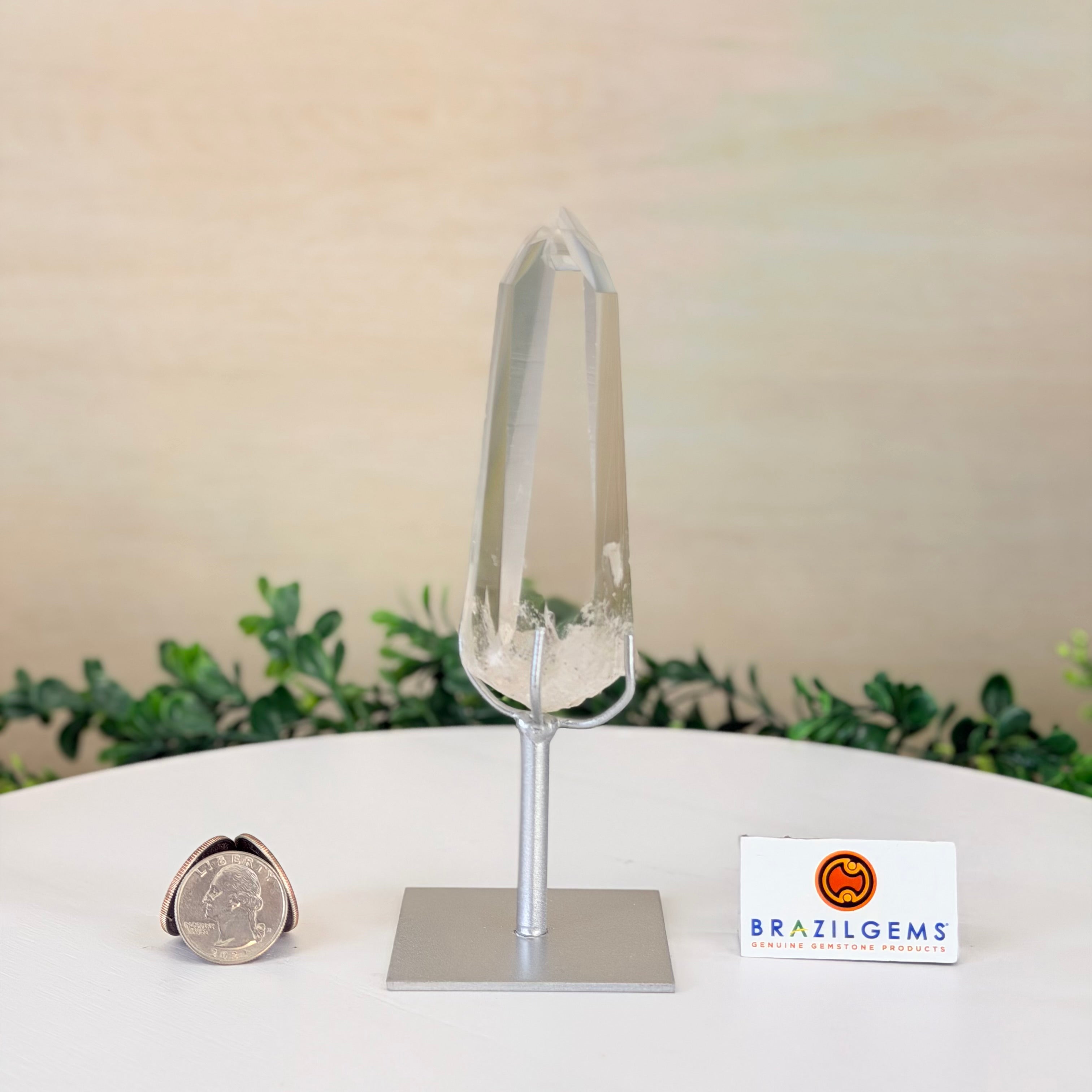 Crystal object on a stand with a small coin for scale, branded 'BrazilGems' on a light background.