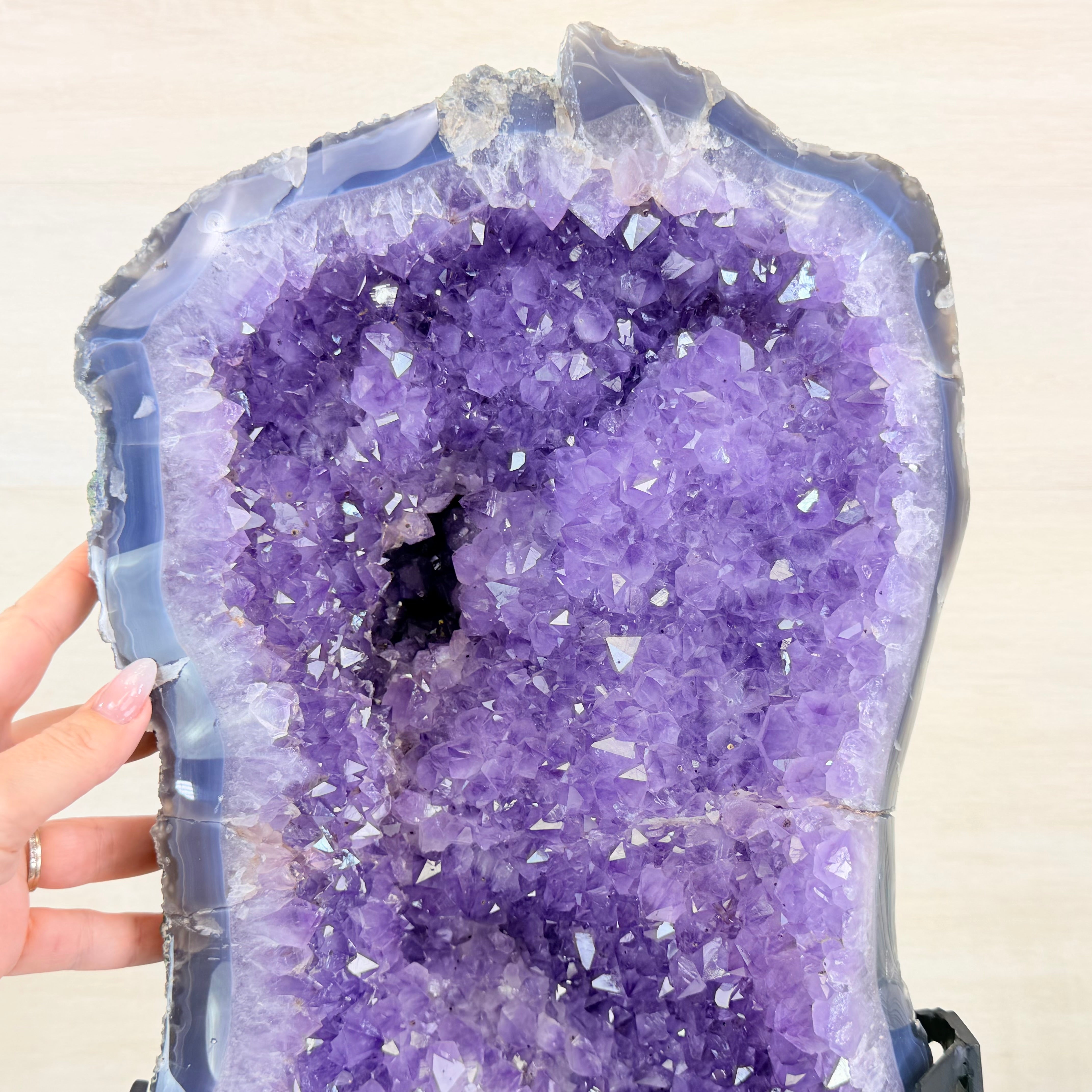 Amethyst crystal cluster held by a hand against a neutral background