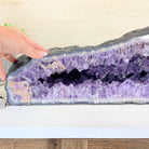 Amethyst geode with a hand touching it on a wooden surface