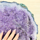 Close-up of a purple crystal geode with a hand for scale on a beige background