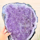 Large purple crystal geode held by a hand against a neutral background