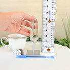 Tea cup with a clear crystal on a stand next to a ruler, with 'BRAZILGEMS' branding.