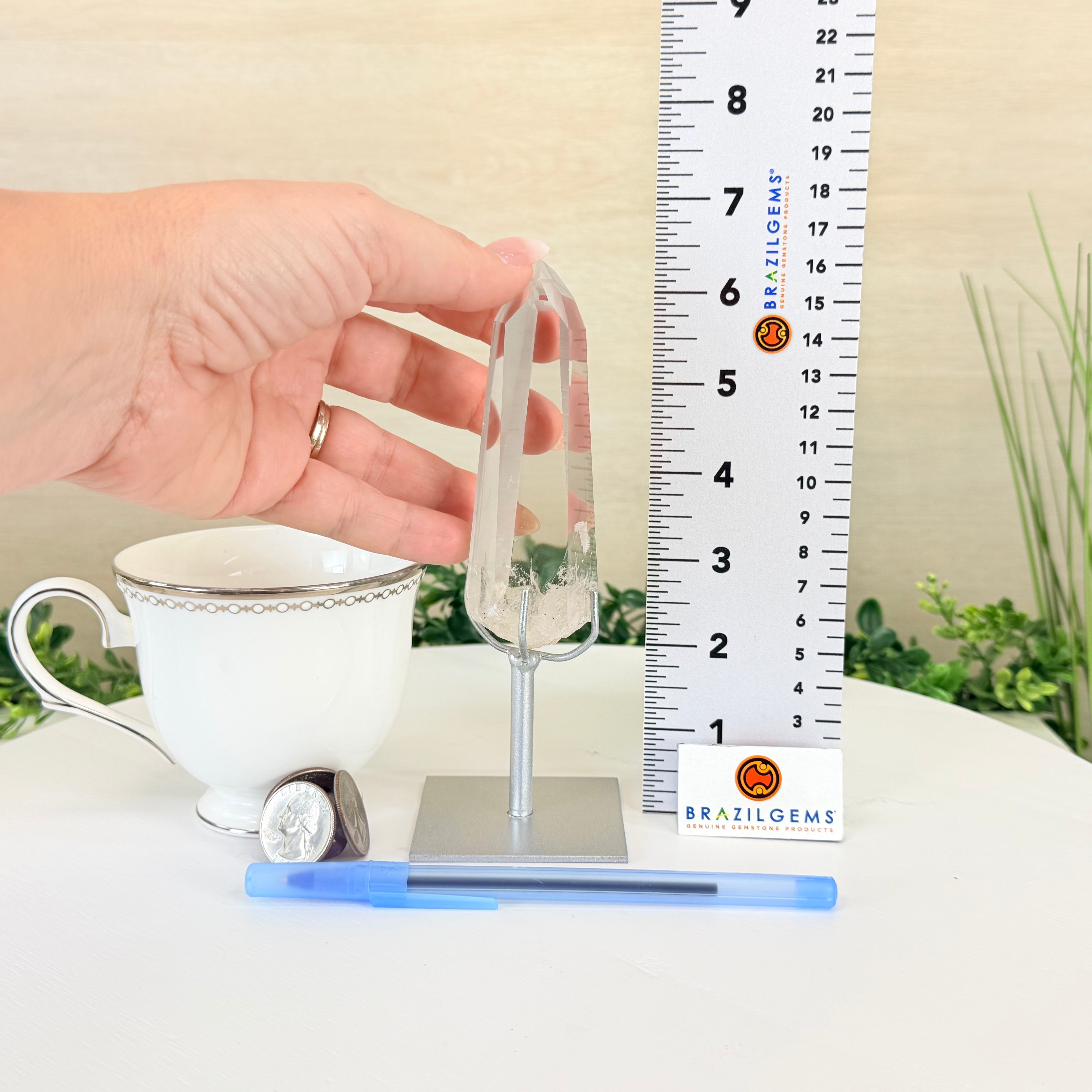 Tea cup with a clear crystal on a stand next to a ruler, with 'BRAZILGEMS' branding.