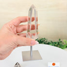 Crystal obelisk held by a hand on a white surface with a blurred background