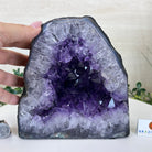 Amethyst crystal geode with a hand for scale on a white surface