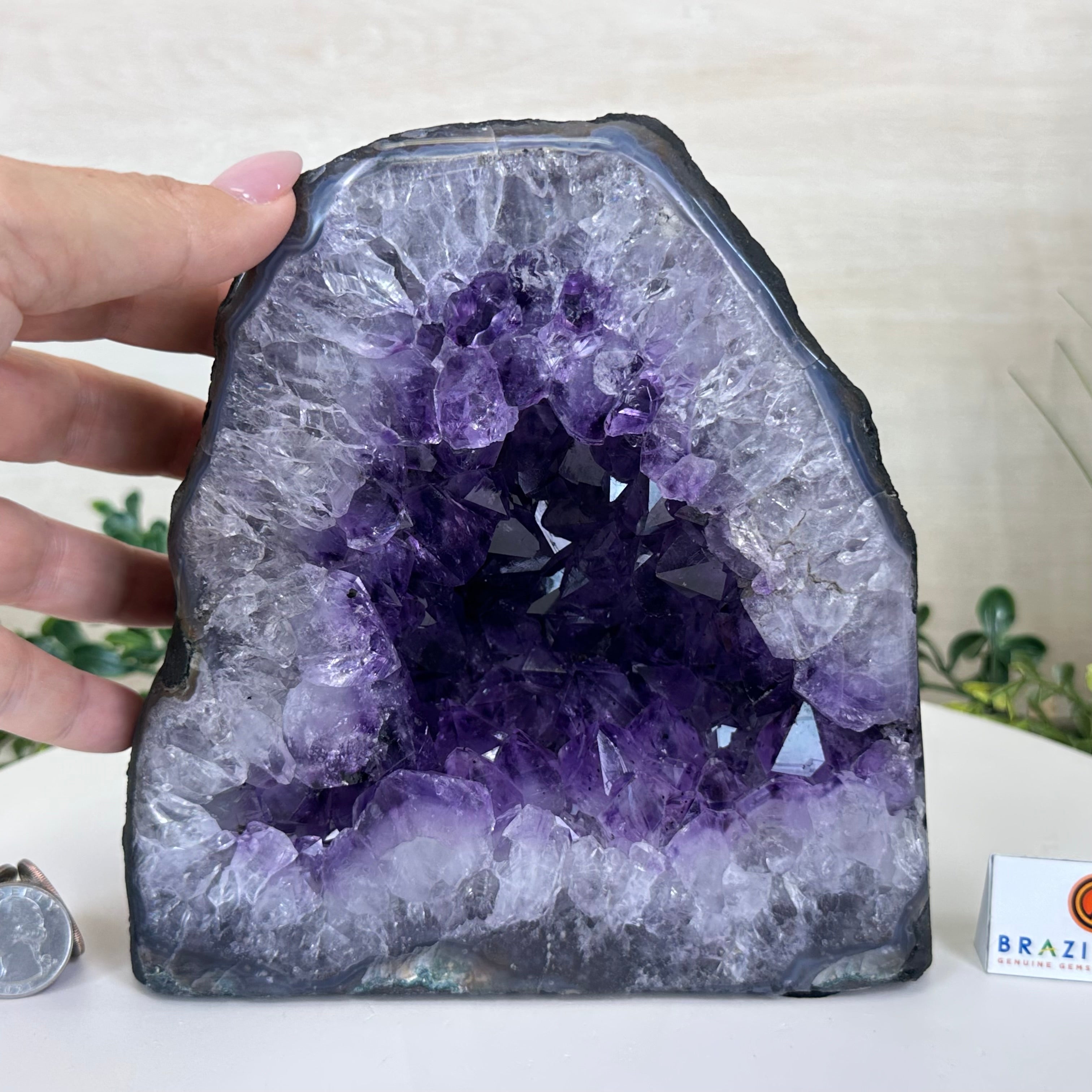 Amethyst crystal geode with a hand for scale on a white surface