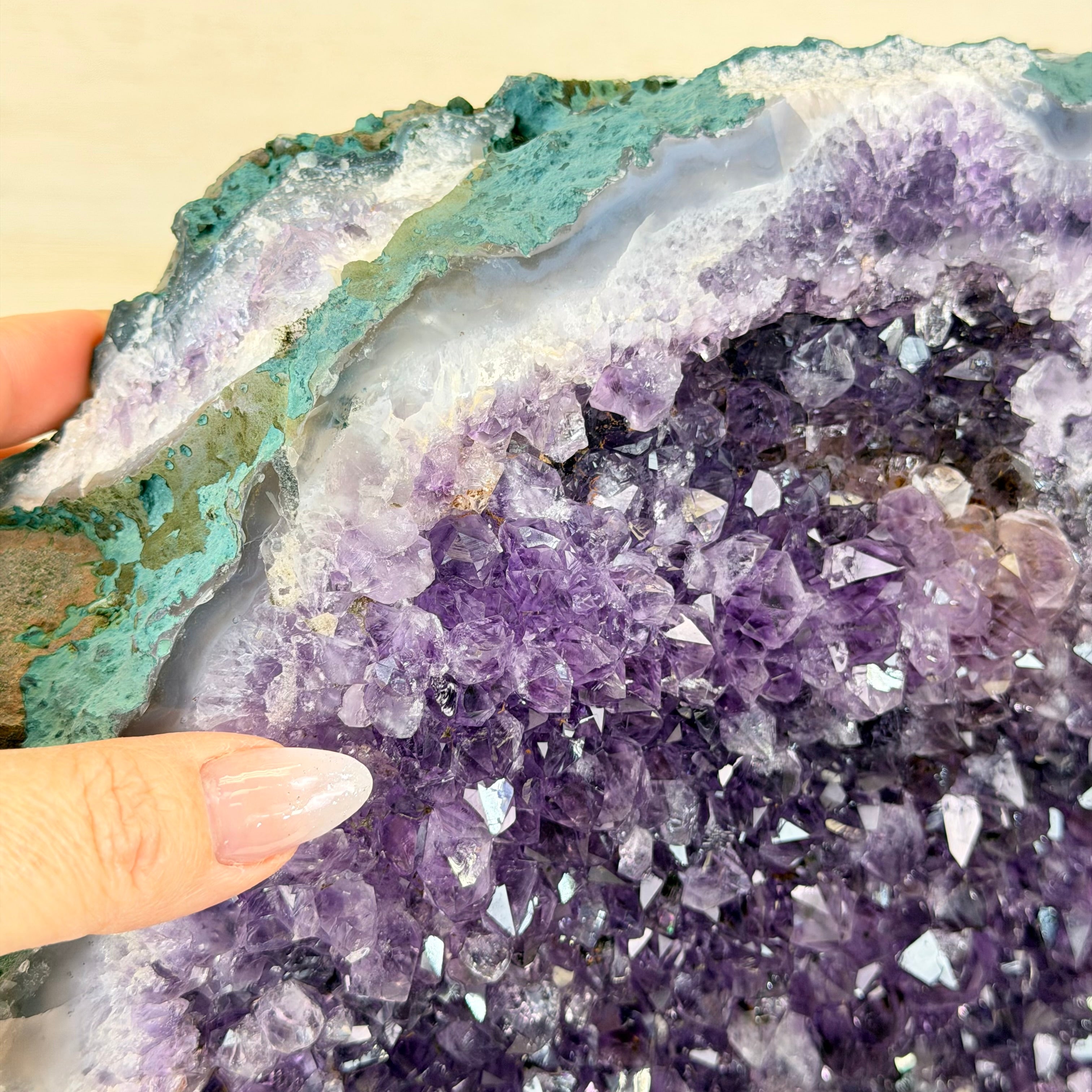 Amethyst crystal formation with a hand for scale on a beige background