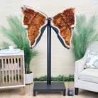 Butterfly-shaped decorative piece on a stand in a living room setting with plants and furniture.