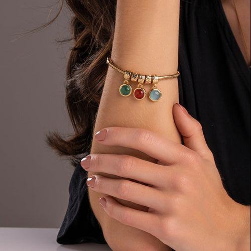 Close-up of a person wearing a gold bracelet with colorful beads on a neutral background