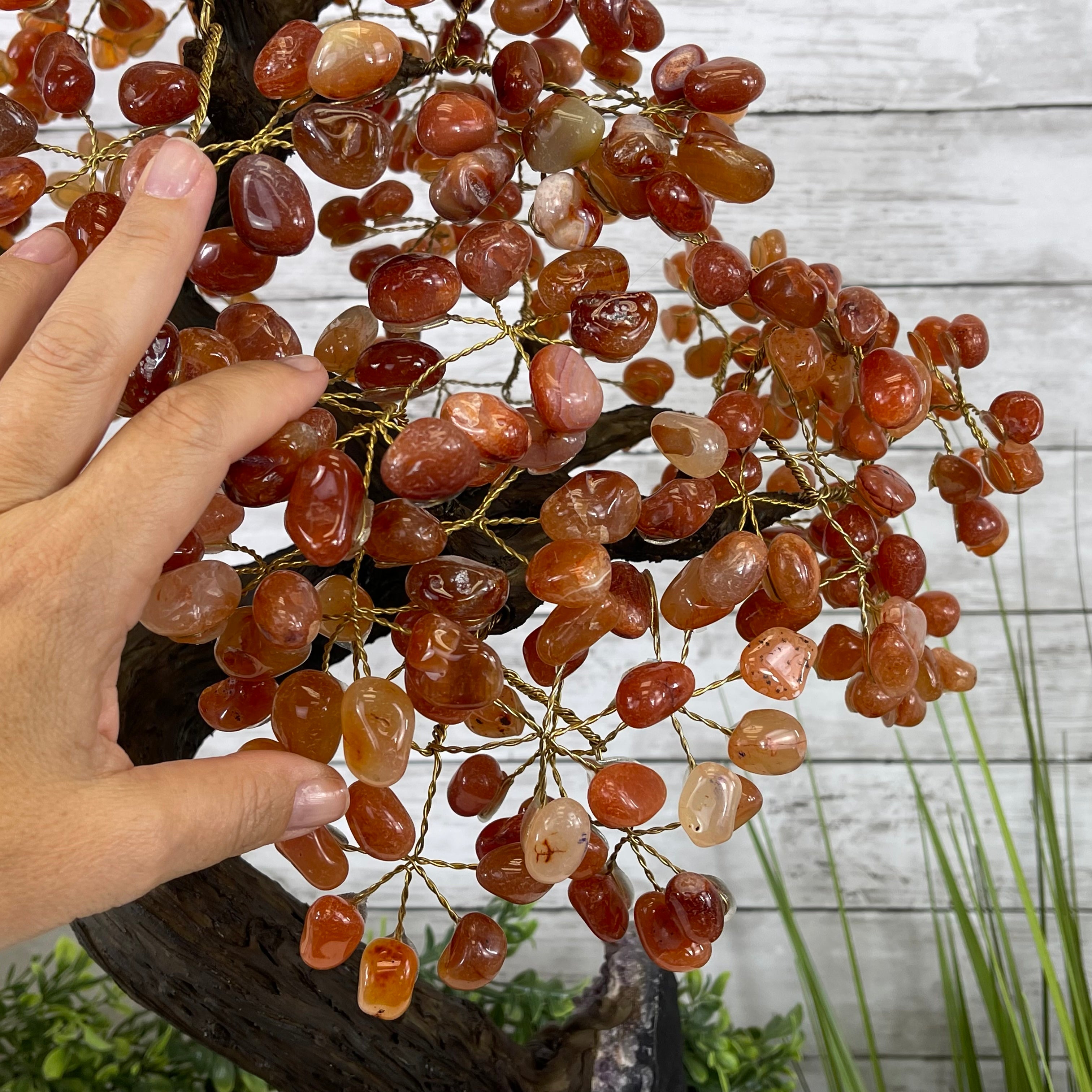 A hand reaching for a handmade Carnelian gemstone tree with red and orange gemstones