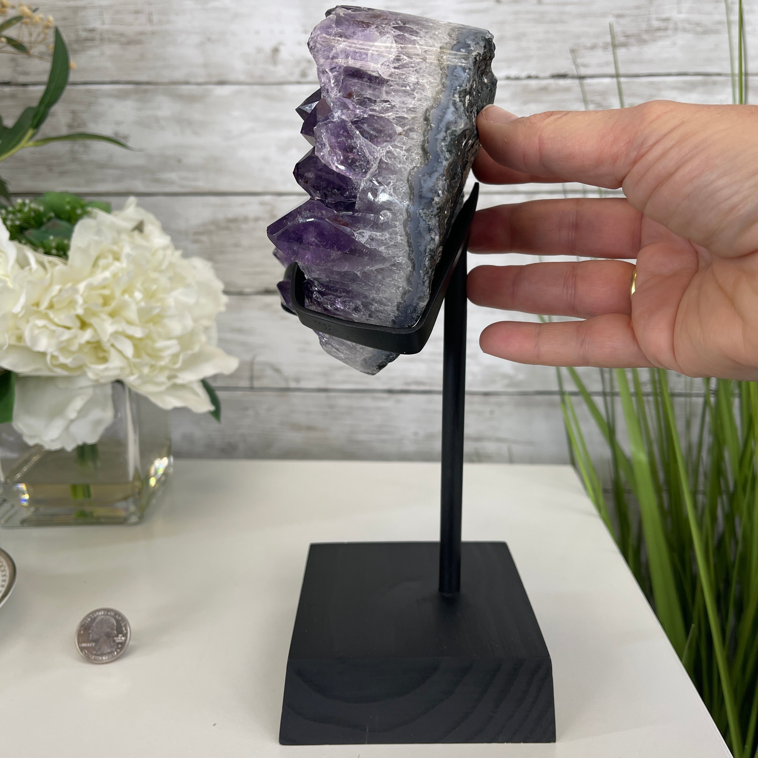 Hand presenting an amethyst heart geode on a black stand